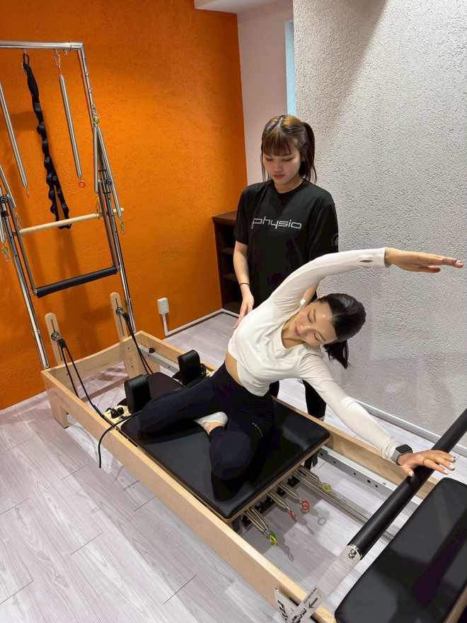 リフォーマーの上に横座りし、腕を伸ばして体側を伸ばす種目